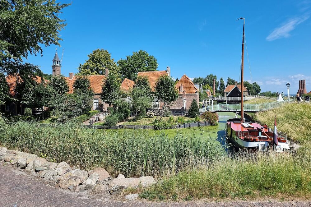 Historische huizen met rode pannendaken aan het water in Enkhuizen, met een houten zeilschip aan de kade en een witte voetgangersbrug