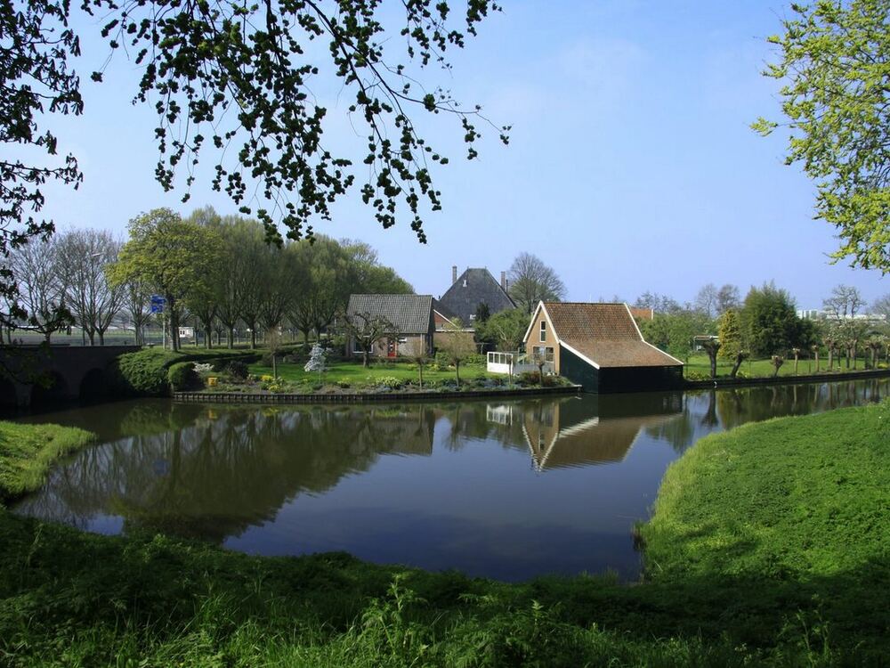 Vestinggracht van Enkhuizen met spiegelend water, groene grasoevers en een huis met rood pannendak aan de overkant